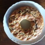 A beautifully baked ricotta and apple Bundt cake (Ciambella) dusted with powdered sugar, sitting on a wooden cutting board, showing the soft texture.