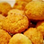 A close-up shot of small, golden-brown coconut cookies arranged on a cooling rack, some dusted with powdered sugar, highlighting the shredded coconut texture.