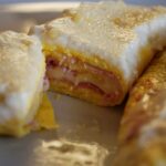Two portions of baked Italian Frittata Rolls stuffed with ham and cheese, covered in a golden brown Béchamel sauce and served in a white baking dish.